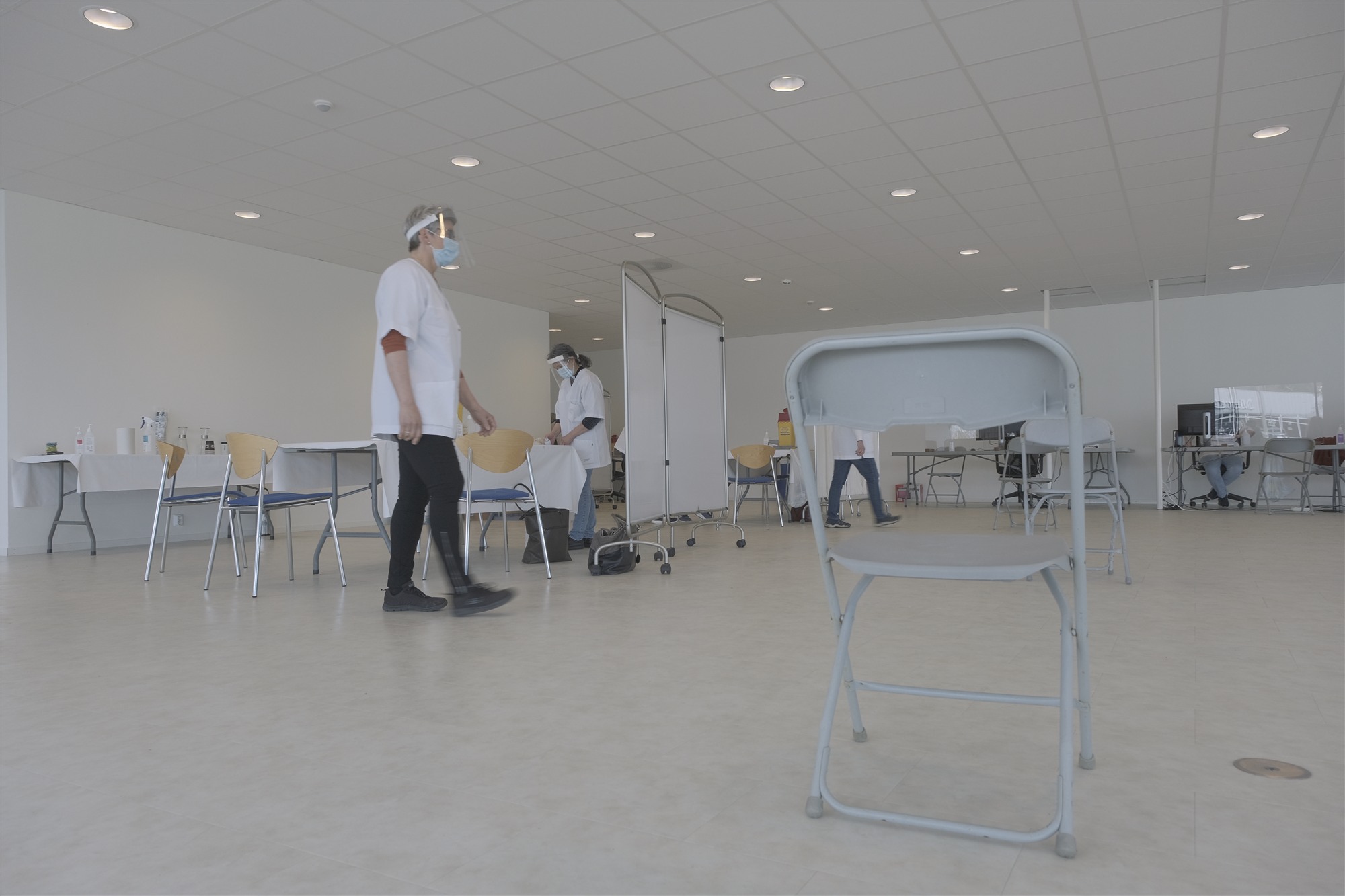 Helsepersonell i visir og munnbind mellom foldestoler og skjermvegger på vaksinesenteret