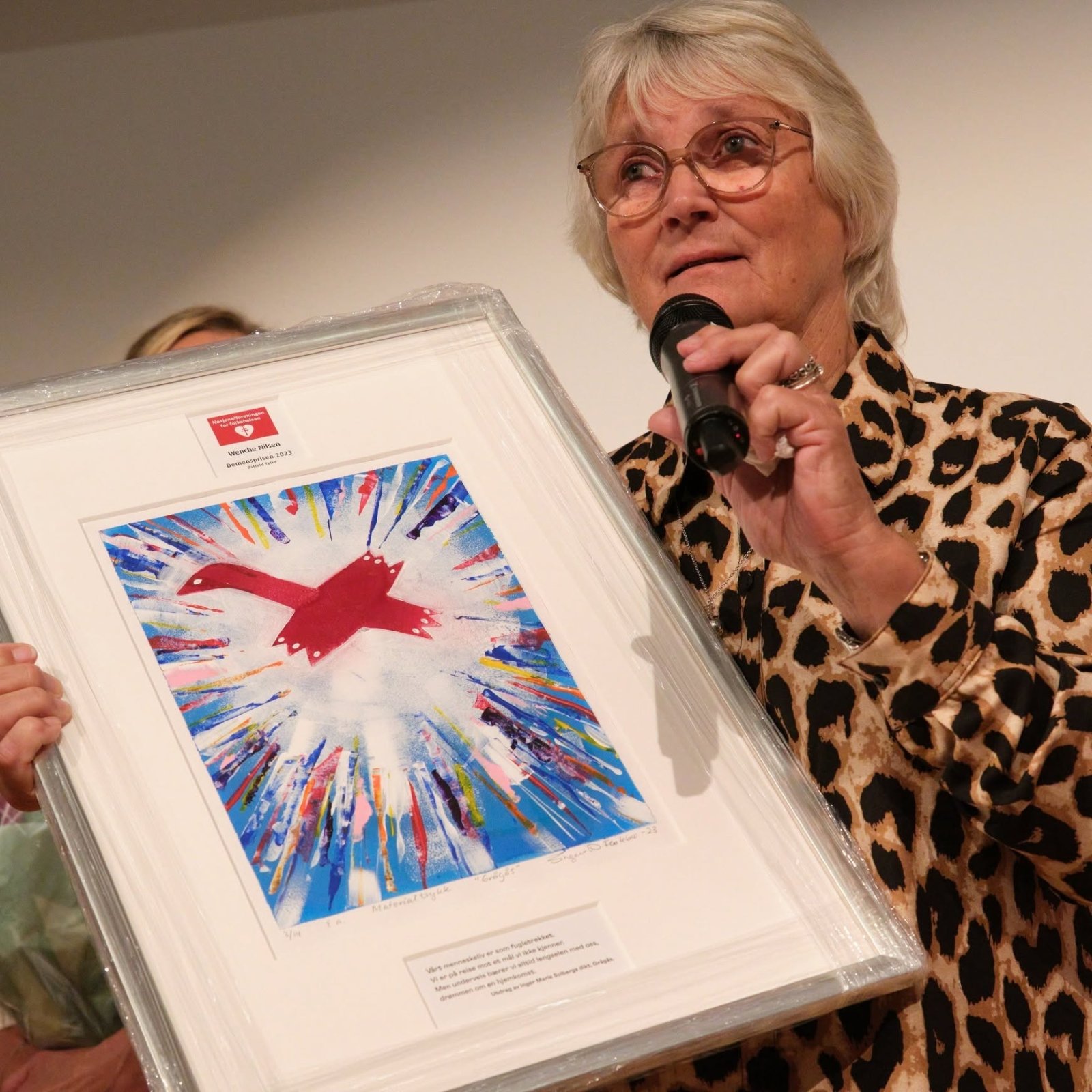 Wenche Nilsen med mikrofon og den innrammede Demensprisen 2023