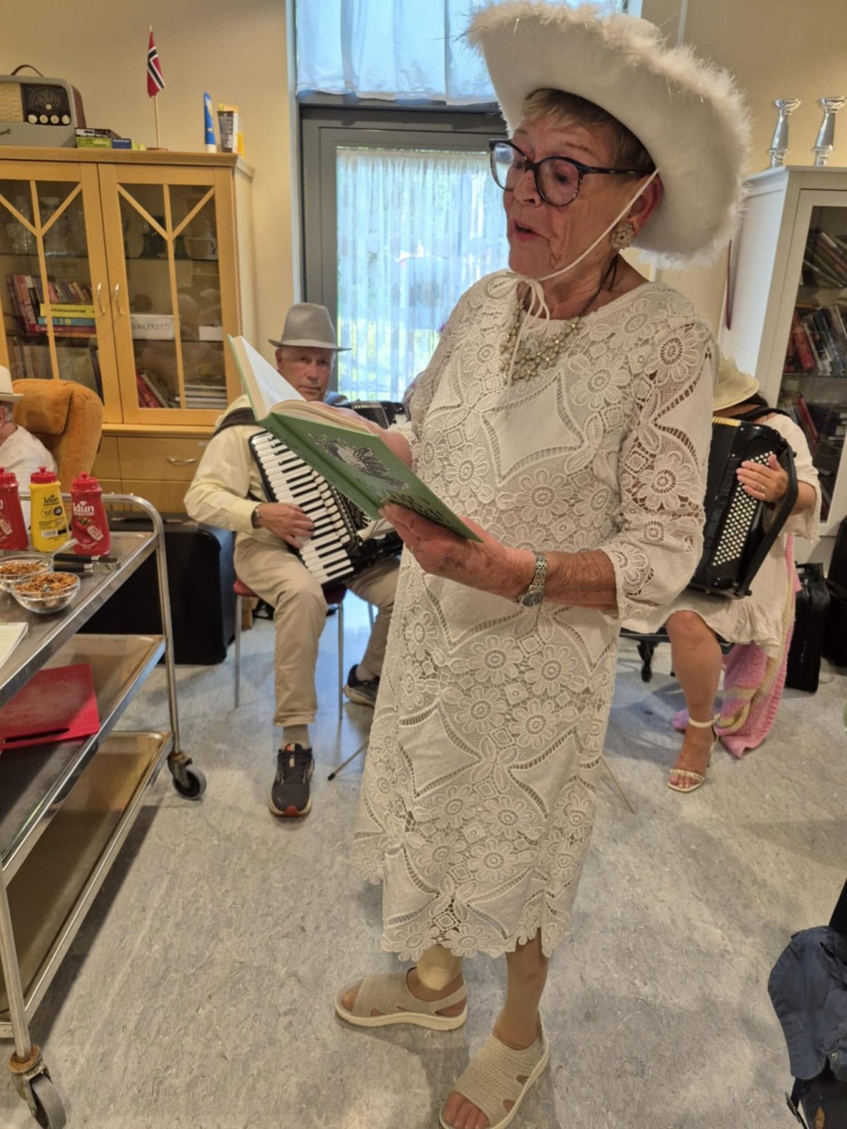 Mariann leder allsangen i hvit kjole og hvit hatt
